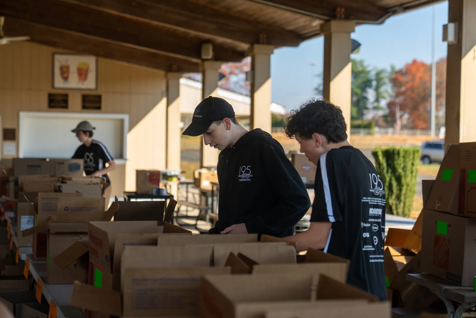 Team 195 students in CyberKnights shirts packing boxes at a community food drive.